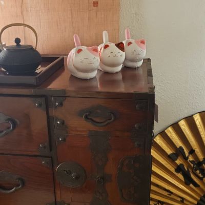 Drei moderne, minimalistisch gestaltete Maneki Neko Glückskatzen in Weiß auf einer antiken japanischen Holzkommode.