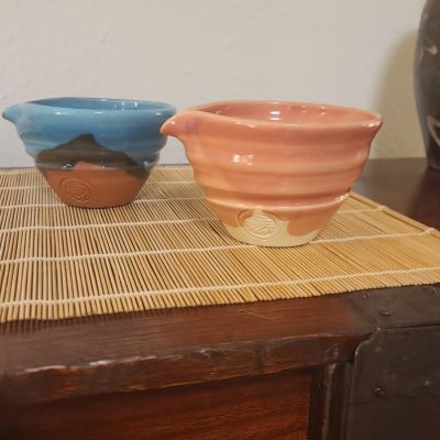 Zwei handgefertigte japanische Keramikschalen aus Kyoto in Blau und Lachsfarben mit sichtbarem Siegel auf einer Bambusmatte.